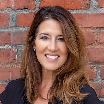 A happy smiling portrait of a woman in front of a brick wall.